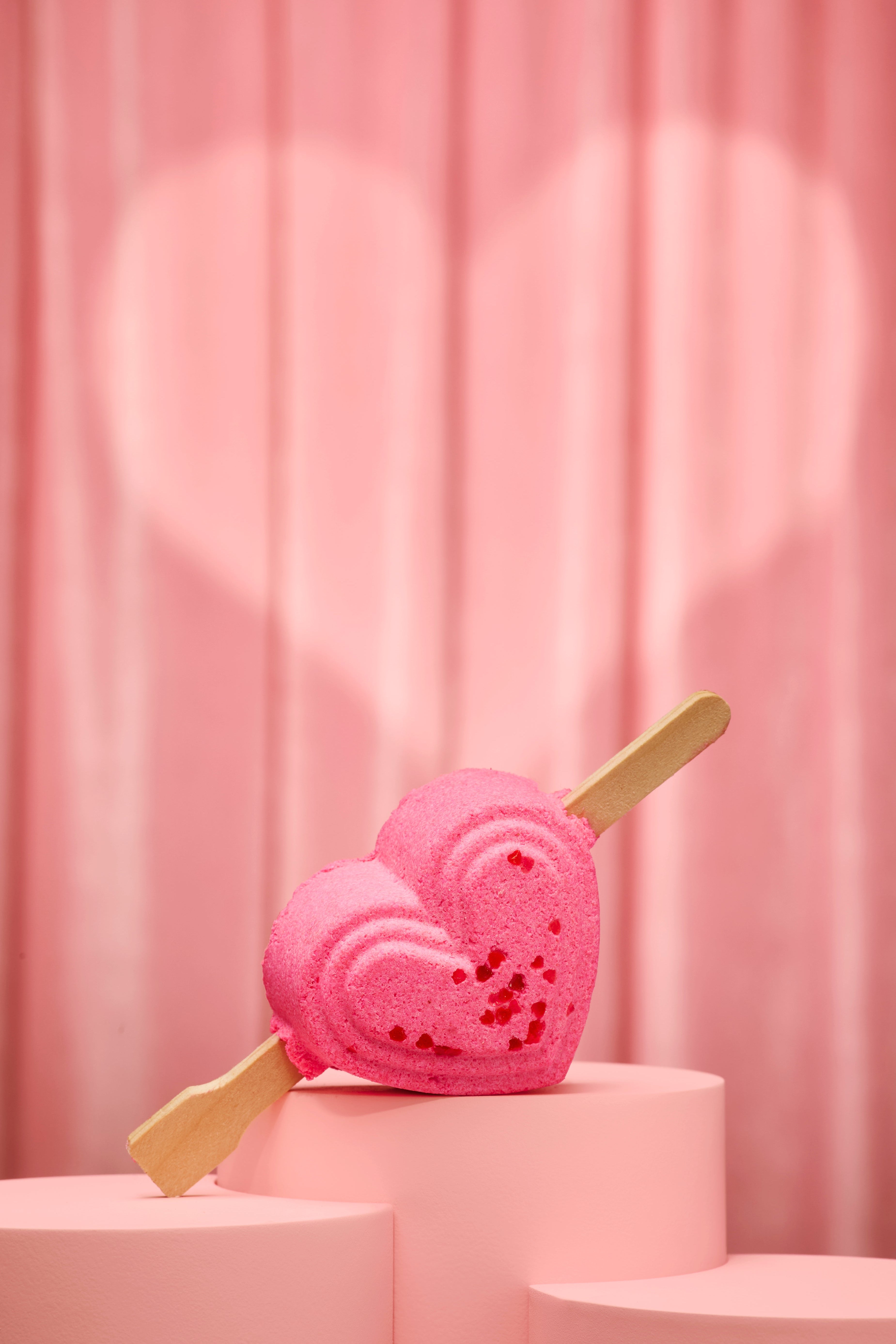 Heart-shaped pink bubble bar with wooden sticks on a pink platform against a pink curtain.