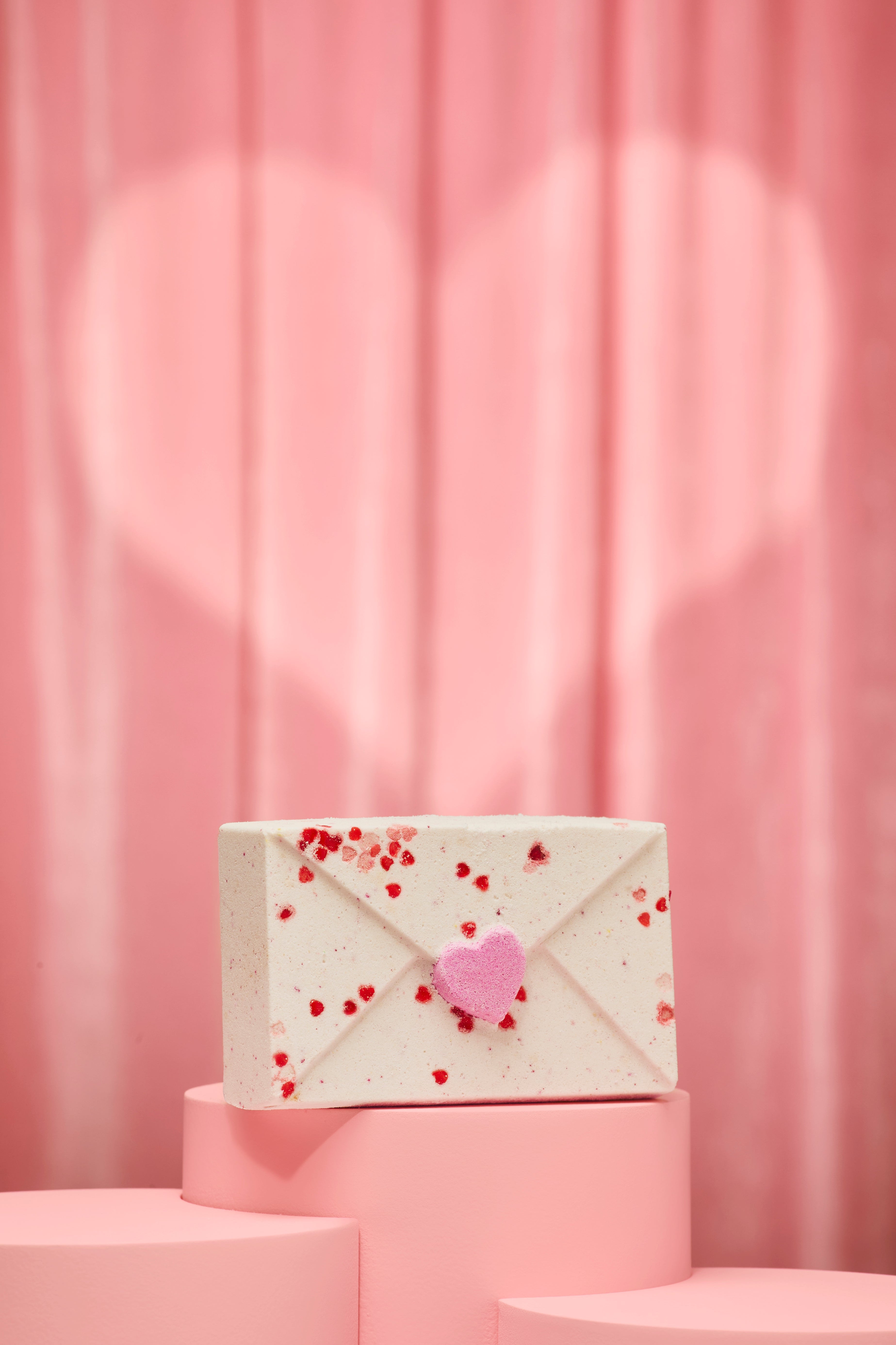 White bath bomb with red heart patterns on a pink background