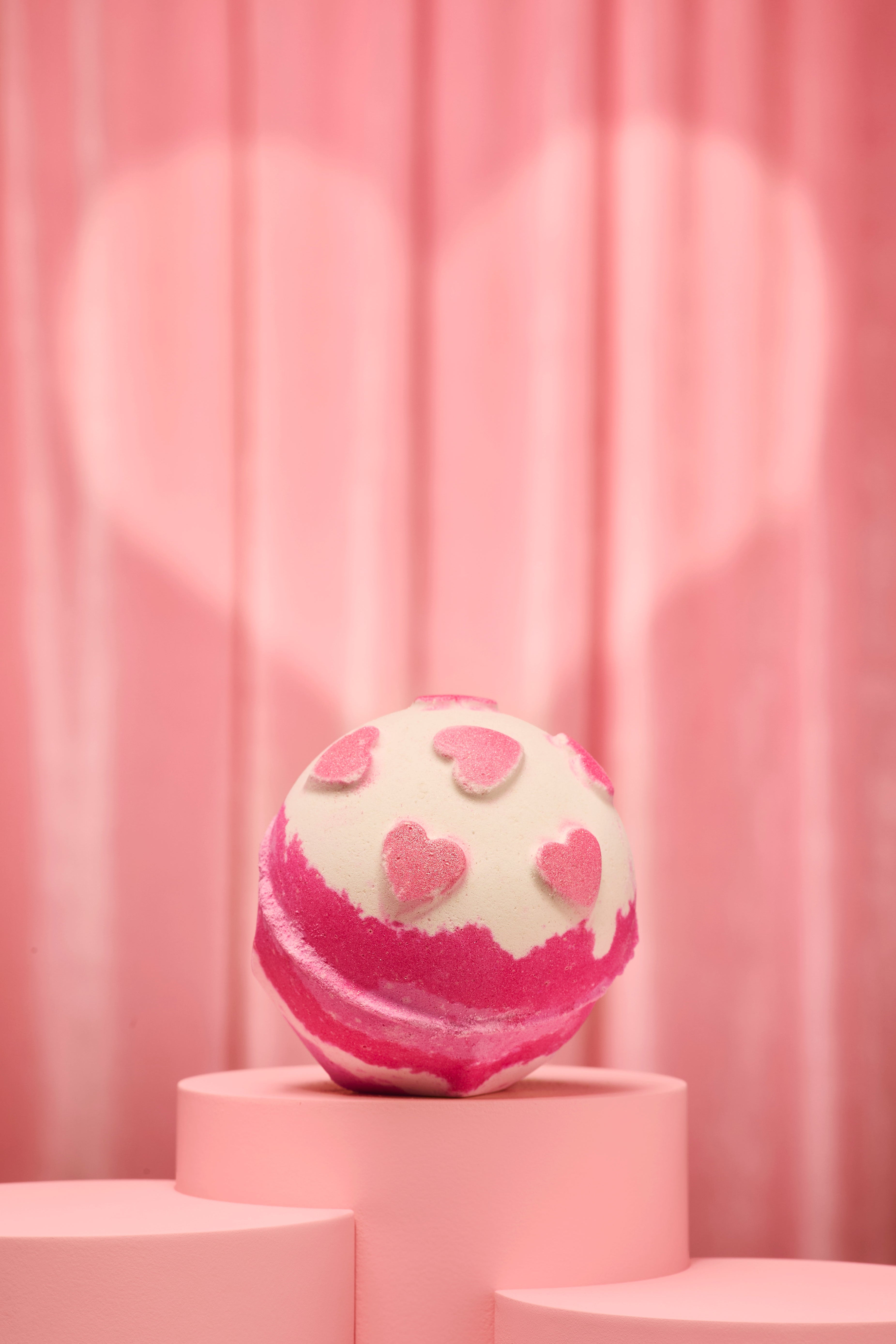 Bath bomb with heart patterns on a pink pedestal against a pink curtain background