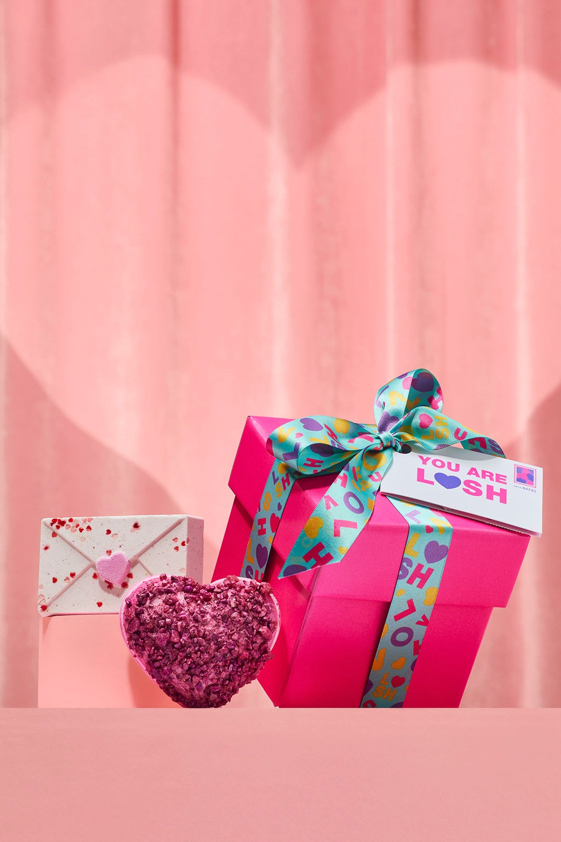 Pink gift box with colorful ribbon and heart-shaped object on a pink background