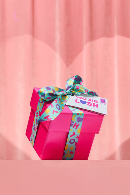 Pink gift box with a colorful ribbon on a pink background